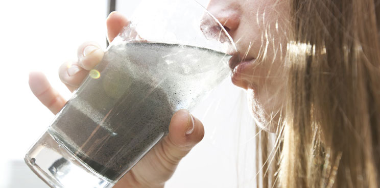 dirty contaminated pfas water in glass particles chemicals blond woman drinking